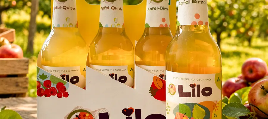 Sechs Flaschen Lilo Apfel-Birne stehen auf einem Tisch im Obstgarten, umgeben von frischen Äpfeln. | © madmoses