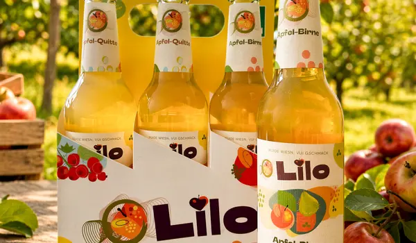 Sechs Flaschen Lilo Apfel-Birne stehen auf einem Tisch im Obstgarten, umgeben von frischen Äpfeln. | © madmoses